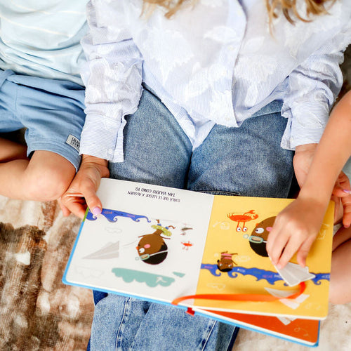 Two children sitting together reading a colorful book with illustrations.