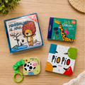 Collection of children's books and toys on a wooden surface with plants in the background.