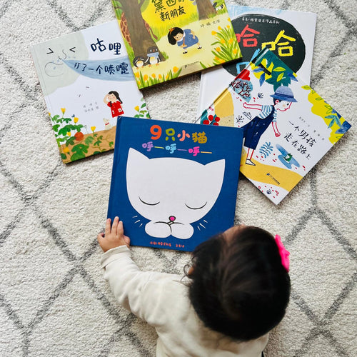 Child interacting with children's Simplified Chinese books on a textured floor
