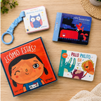 Collection of children's books and toys on a wooden surface with plants in the background.